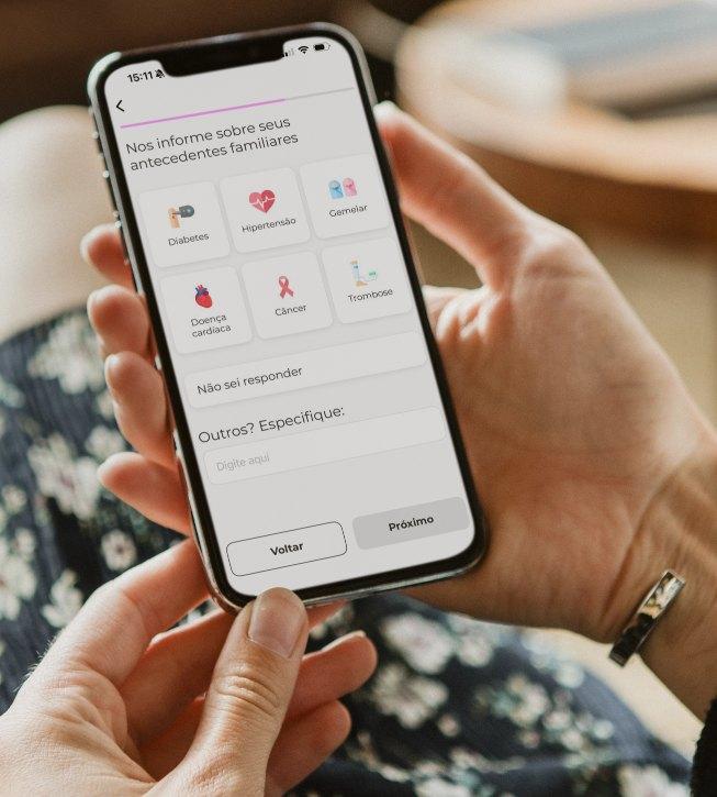 Mãos segurando o celular com o questionário de antecedentes familiares do app Mãe-Estar